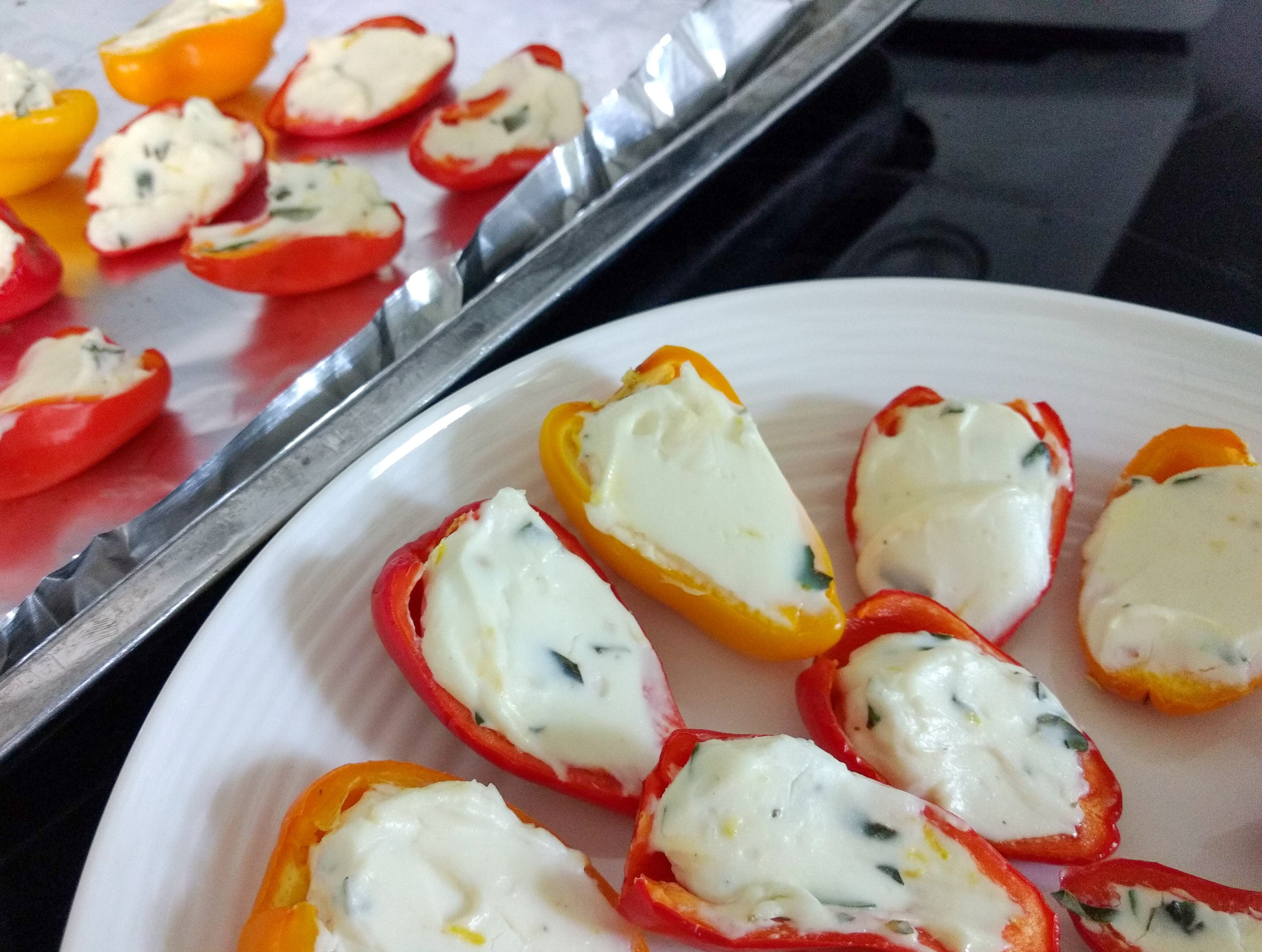 herb and cream cheese stuffed mini yellow and red peppers on a baking pan to the left and more in a white plate to the right